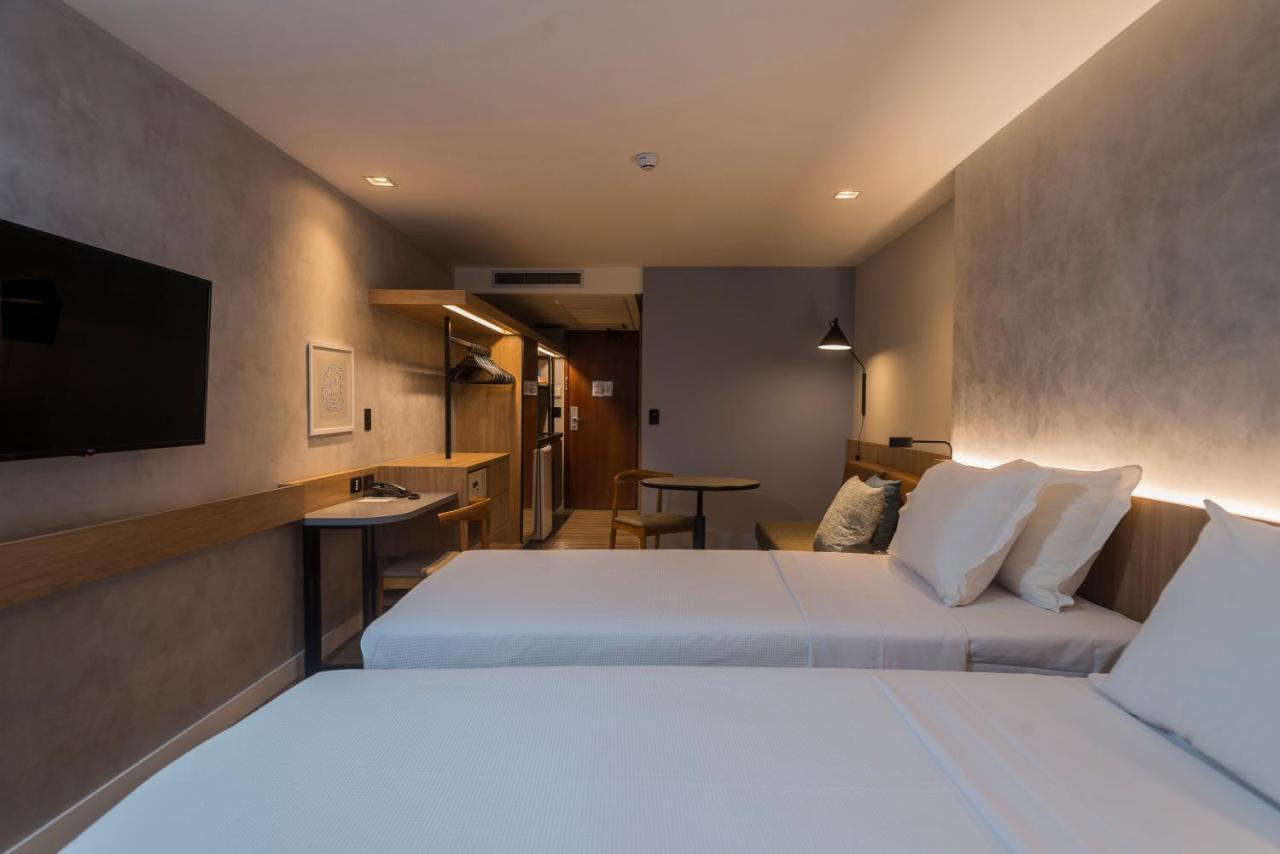 Hotel Luzeiros Fortaleza 외부 사진 The photo shows a hotel room with a modern and minimalist design. There are two single beds with white linens and pillows placed next to each other. A wall-mounted flat-screen TV is positioned above a small table or desk area, which has a wooden fini