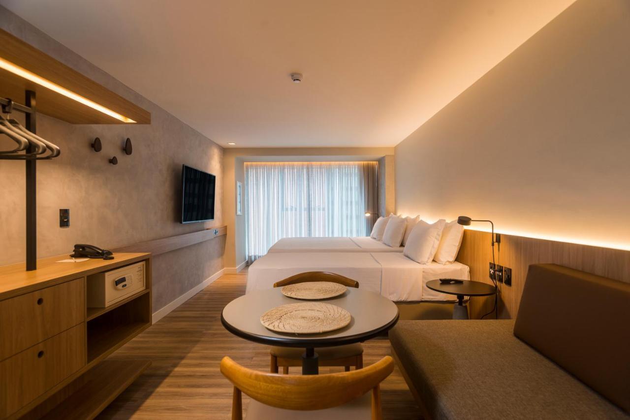 Hotel Luzeiros Fortaleza 외부 사진 The photo shows a modern hotel room with a clean and minimalist design. It features two beds with white bedding positioned against a wall. There is a large window with sheer curtains allowing natural light to fill the space. Opposite the beds, a flat