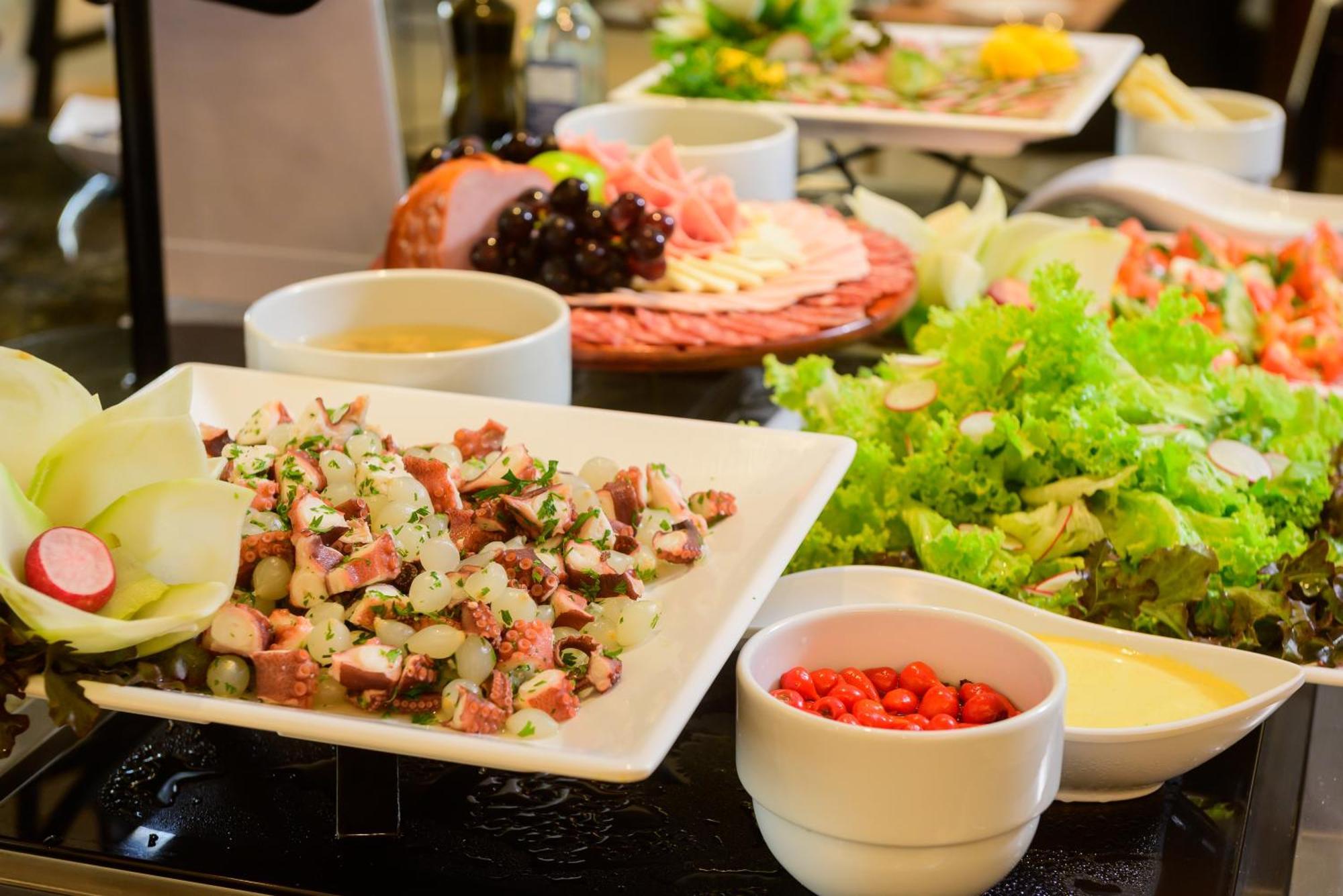 Hotel Luzeiros Fortaleza 외부 사진 The photo shows a variety of food items arranged on a table. In the foreground, there is a white plate with a mixed dish that includes chopped ingredients, likely vegetables and possibly meat, garnished with herbs. Surrounding this dish are several b