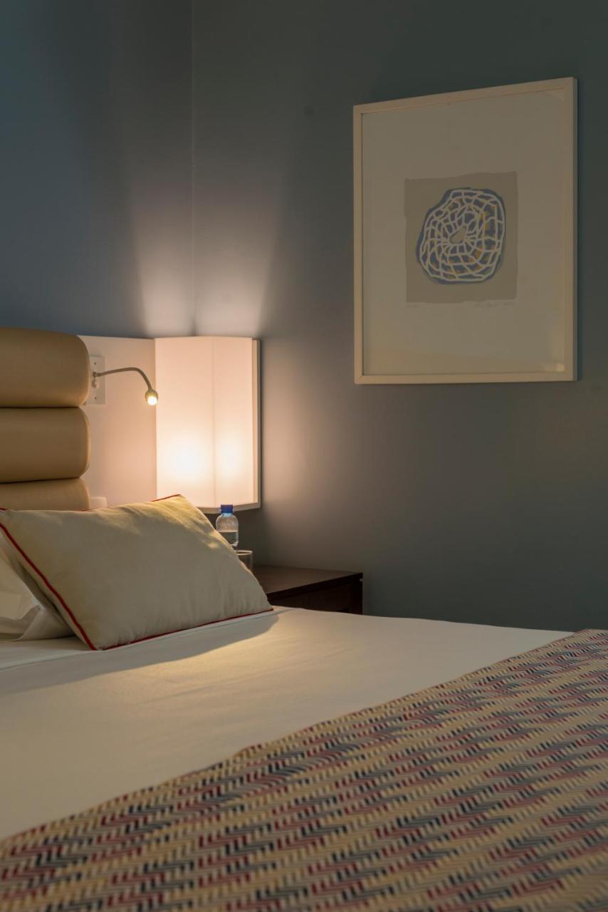 Hotel Luzeiros Fortaleza 외부 사진 The photo shows a cozy bedroom setting. There is a neatly made bed with a white sheet and a couple of decorative pillows. One of the pillows is slightly displaced. On the bedside table, there is a small bottle of water and a lamp with a warm glow. Th